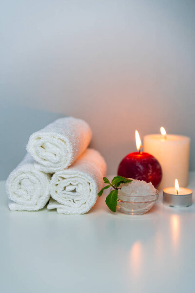SPA session at salon vertical photo on grey background with stack of towels, candle lights and cup of sea salt.