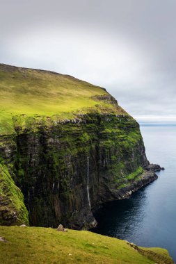 Faroe Adaları 'ndaki Gjogv köyündeki yürüyüş yolunda şelale okyanusa düşüyor..