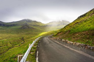 Gökyüzü bulutlu yeşil dağlarla kaplı bir yolculuk fotoğrafı. Faroe Adaları, Danimarka.