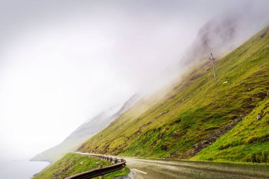 Faroe Adaları 'nda yol gezisi. Bulutlu gökyüzü ve fiyort boyunca uzanan yeşil dağlarla olağanüstü manzara fotoğrafı.. 