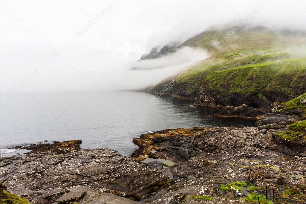 Vidareidi village bay landscape with green mountains covered with thick fog. Faroe Islands, Denmark. 