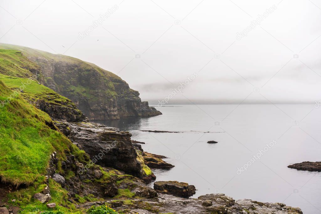 Green cliffs above the ocean with great overcast sky after rain. Faroe Islands landscape, Denmark.