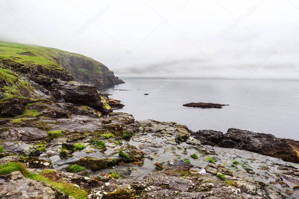 Foggy landscape on one of Faroe Islands with green hills, fjord, and great overcast sky.