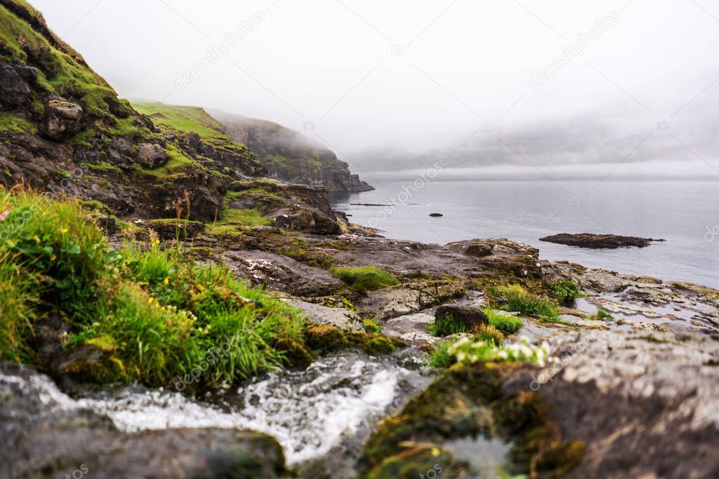 Water stream flowing into the ocean in Vidareidi village, Faroe Islands. Great overcast sky and green hills. 