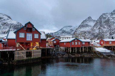 Lofoten Köyü. Kışın geleneksel kırmızı rorbu evleri ve karlı dağlarla..