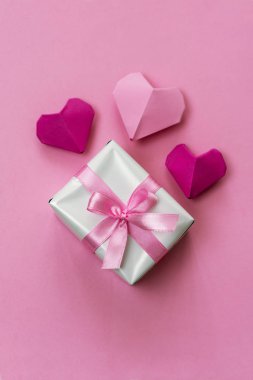 Origami kalpleri ve pembe kurdeleyle sarılı bir hediye kutusu. Sevgililer Günü tasarımları için ideal..