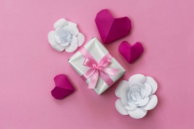 Romantik hediye düz fotoğraf pembe kurdele, origami kalpleri ve beyaz kağıt çiçeklerle sarılı bir kutu ile yatıyordu..