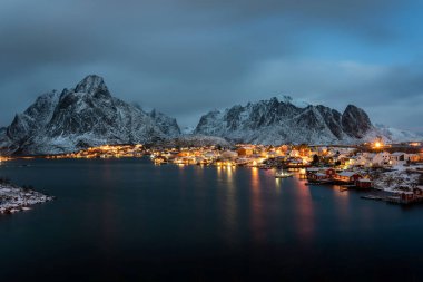 Reine Köyü geceleri, binanın ışıkları ve karlı dağlarıyla dolu. Lofoten Adaları, Norveç.