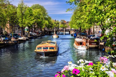 Amsterdam, Hollanda - 23 Mayıs 2019: Güneşli bahar aylarında turist tekneleri ve geleneksel Hollanda binalarının bulunduğu şehir kanalı manzarası.