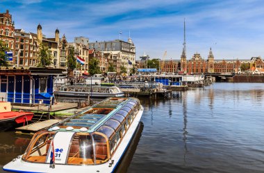 Amsterdam, Hollanda - 23 Mayıs 2019: Damrak caddesinden gelen teknelerle kanal manzarası. Arka planda Centraal İstasyonu var..