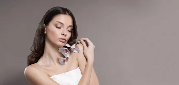 Ung och frisk kvinna med lätt make-up håller orkidé blomma. Beige bakgrund. — Stockfoto