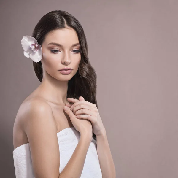 Donna giovane e sana con trucco leggero e fiore di orchidea. Sfondo beige . — Foto Stock