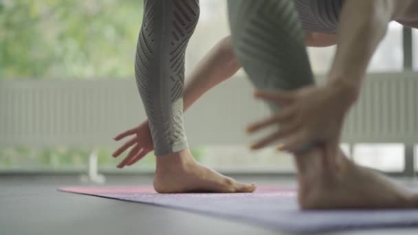 Атлетическая женщина наклоняется вперед с широко раскинутыми ногами в позе йоги Прасарита Падоттанасана — стоковое видео