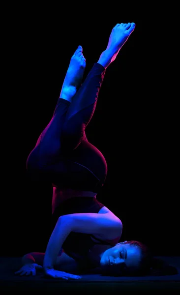 Young fit woman practicing yoga. Neon light. Modern sci fi representation of yoga. Calm and tranquil atmosphere