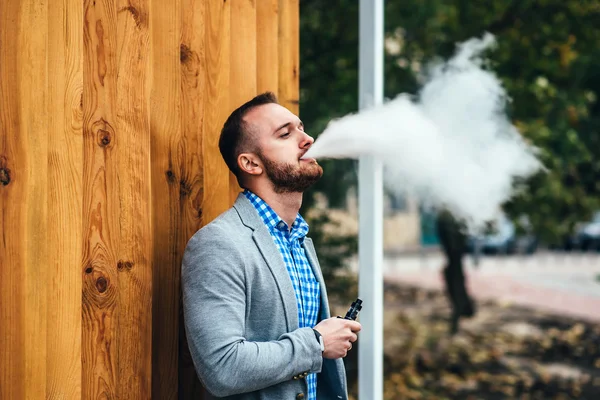 Человек с бородой испаряющий электронную сигарету — стоковое фото