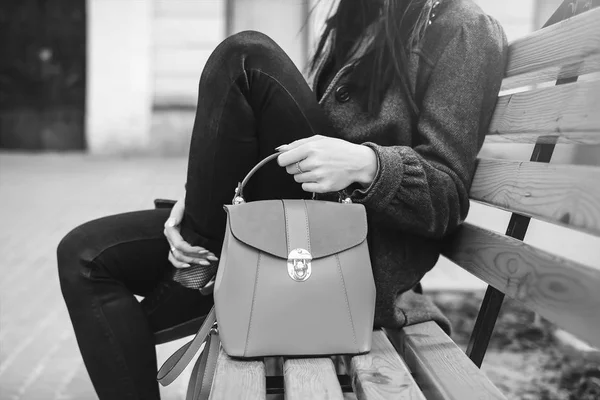 Kvinna sitter på bänken med väska i händer, svart och vitt — Stockfoto