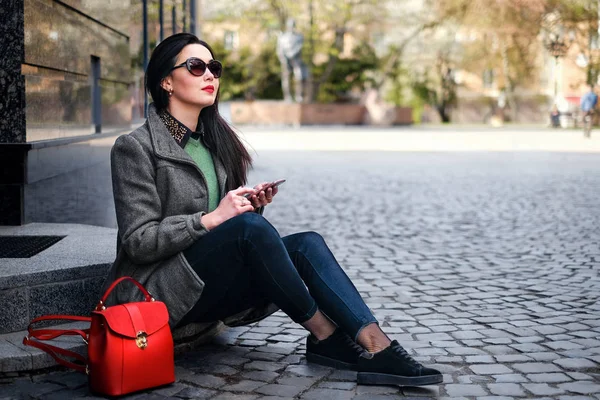 Brunette dívka sedící na ulici s mobil — Stock fotografie