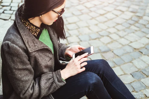 Chica morena sentada en la calle con teléfono celular —  Fotos de Stock