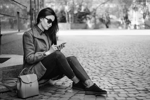 Meisje zittend op straat met mobiele telefoon — Stockfoto