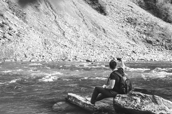 Yong путешественник делает фото возле горной реки, черно-белый — стоковое фото