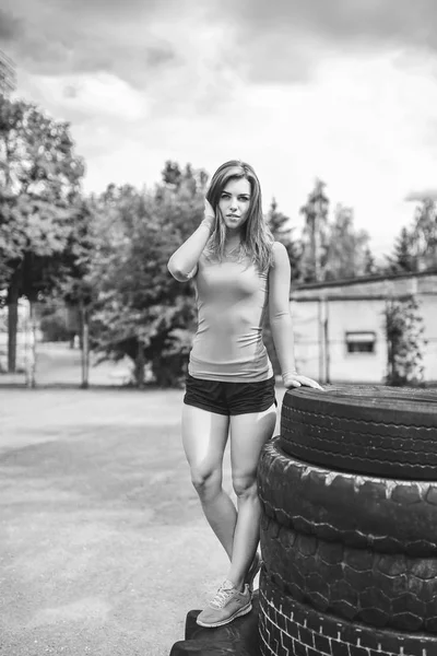 Menina bonita desportiva perto de pneus enormes ao ar livre, preto e branco — Fotografia de Stock