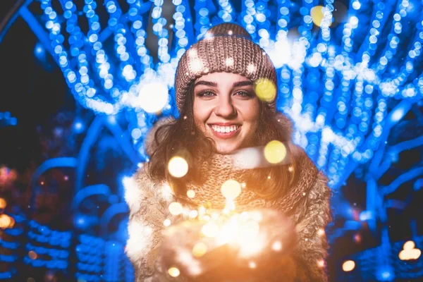 カメラ目線のクリスマス ライトを保持しているニットの帽子で微笑んでいる女の子の屋外のポートレート — ストック写真