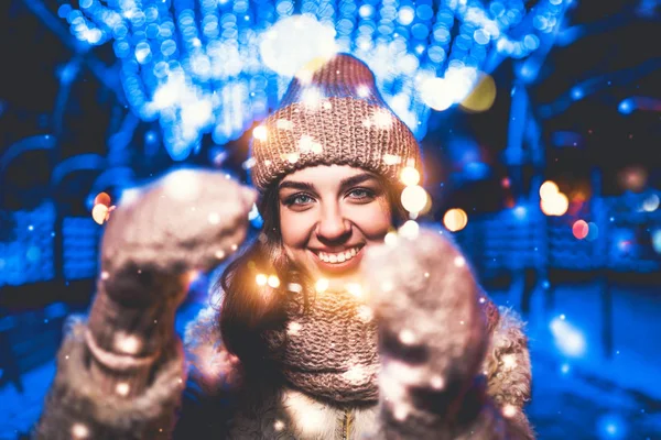 ニット帽子クリスマス ライトを押しながらカメラ目線で微笑んでいる女の子の屋外のポートレート — ストック写真