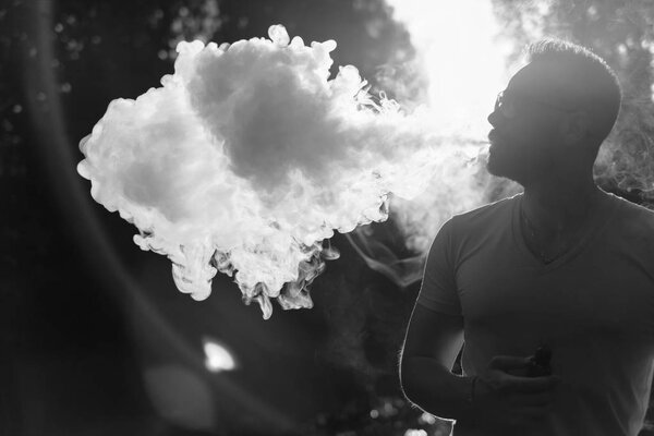 Man with beard smoke electronic cigarette outdoor, black and white