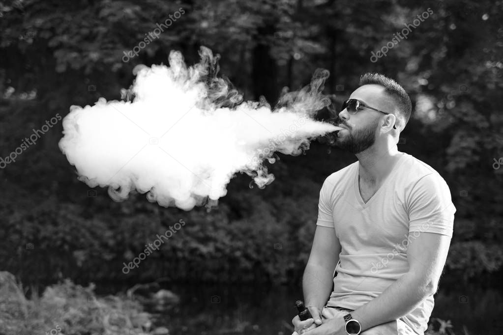 Man with beard smoke electronic cigarette outdoor, black and white