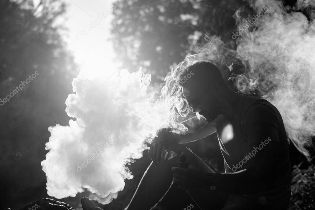 Man with beard smoke electronic cigarette outdoor, black and white
