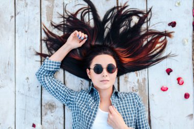 Güzel esmer kız kırmızı gül yaprakları ile ahşap zemin üzerinde rahatlatıcı güneş gözlüğü