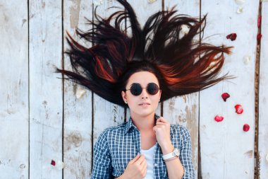 Güzel esmer kız kırmızı gül yaprakları ile ahşap zemin üzerinde rahatlatıcı güneş gözlüğü