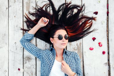 Güzel esmer kız kırmızı gül yaprakları ile ahşap zemin üzerinde rahatlatıcı güneş gözlüğü