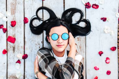 Güzel esmer kız kırmızı gül yaprakları ile ahşap zemin üzerinde rahatlatıcı güneş gözlüğü