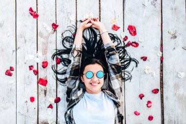 Güzel esmer kız kırmızı gül yaprakları ile ahşap zemin üzerinde rahatlatıcı güneş gözlüğü