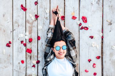 Güzel esmer kız kırmızı gül yaprakları ile ahşap zemin üzerinde rahatlatıcı güneş gözlüğü