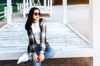 Ahşap katta oturan ve parkta açık rahatlatıcı güneş gözlüklü genç esmer kadın