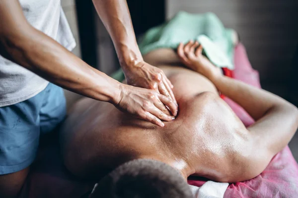 En kvinnlig sjukgymnast som masserar ryggen åt en man på läkarmottagningen. Närbild av händer som gör massage — Stockfoto