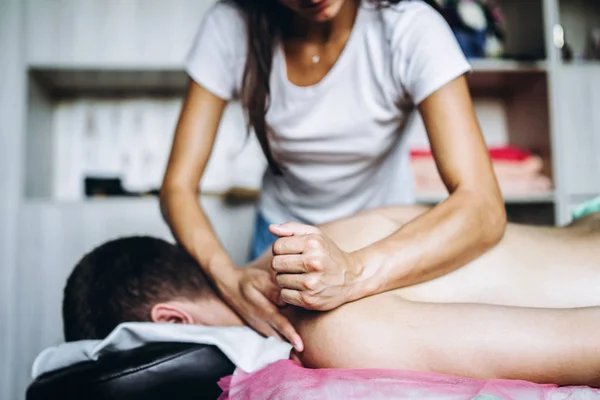 Kvinnlig massös ger tillbaka massage till mannen som ligger på massagesoffan — Stockfoto