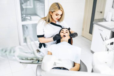 Ofisinde çalışan bir dişçi. Siyah eldiven giyen bir kadın doktor klinikteki hastayı muayene ediyor. Sağlık ve Tıp Konsepti