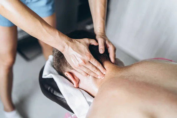 En kvinnlig sjukgymnast som masserar nacken för en man på läkarmottagningen. Närbild av händer som gör massage — Stockfoto