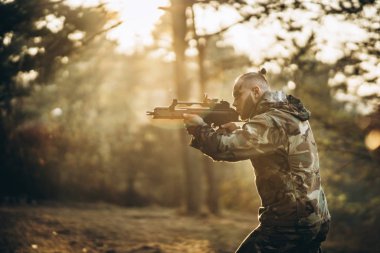 Bir kamuflaj askeri ormanda hava yumuşaklığıyla oynuyor.