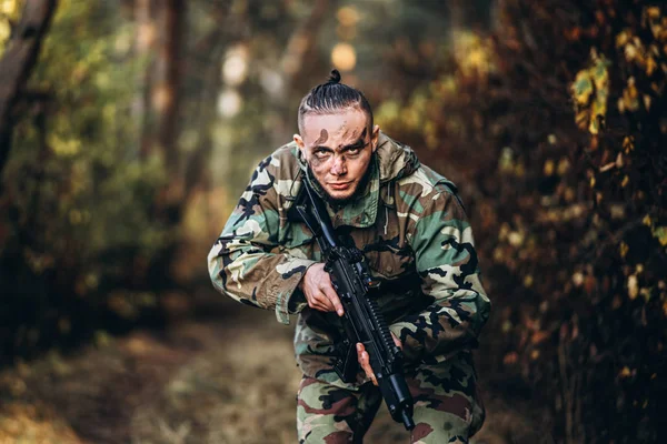 Porträt eines Tarnsoldaten mit Gewehr und gemaltem Gesicht, der im Freien im Wald spielt — Stockfoto