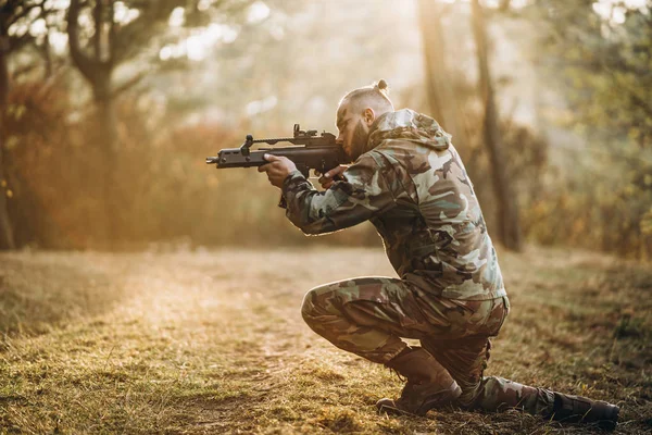 Een camouflage soldaat die buiten luchtzacht speelt in het bos, op één knie staat, mikt op het geweer — Stockfoto