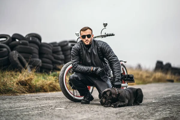 Biker in a leather suit crouched near his dog and red motorcycle