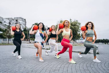 Bir grup sportif kadın kameraya poz veriyor, egzersiz yapıyorlar.