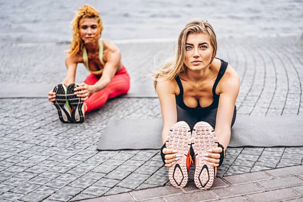 Дві жінки практикують вправи йоги на килимку на вулиці поруч з — стокове фото