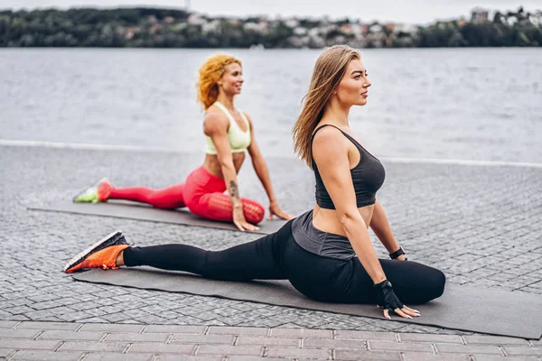 Zwei Frauen praktizieren Yoga-Übungen auf einer Matte auf der Straße in der Nähe von — Stockfoto