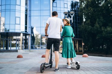 Siyah beyaz elektrikli scooterlı bir adam ve kadın. Arkadan bak. C