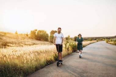 Tatildeki genç çift kırsal kesimde yolda elektrikli scooter sürerken eğleniyor. İçerik teknolojileri. Boşluğu kopyala